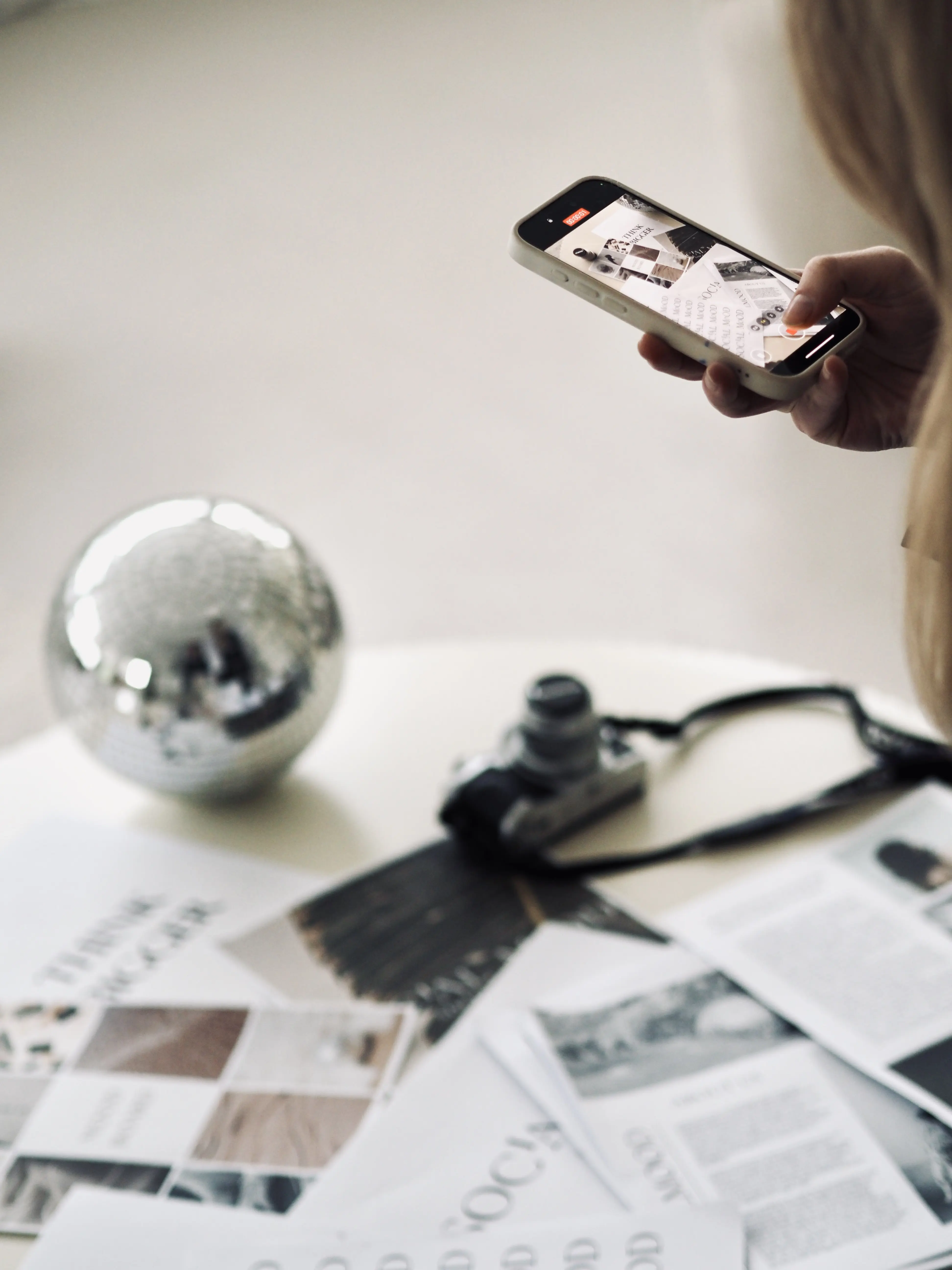 Eine Person fotografiert mit einem Smartphone einen Tisch, auf dem eine Kamera, eine Diskokugel und verschiedene Bilder liegen, symbolisch für Content Creation.